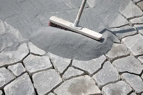 Besen verteilt feinen Fugensand auf Pflastersteinen. Der Sand dient als effektiver Fugensand gegen Unkraut und stabilisiert die Steine.